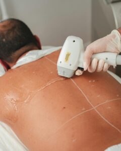 A professional performing laser hair removal on a male client in a beauty clinic.